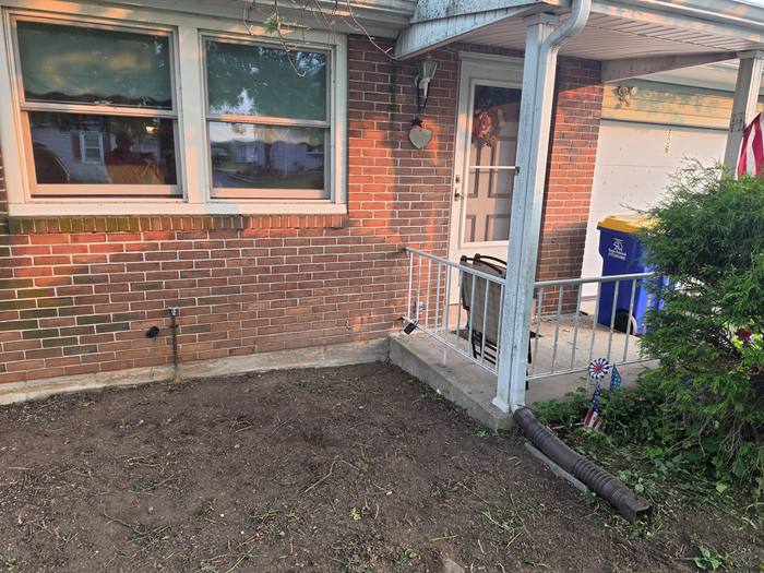 Front entrance of a brick ranch home before deck construction, with concrete stoop, metal handrail and bare soil — Richland, PA